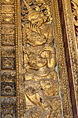 Wat Xieng Thong temple in Luang Prabang, Laos. Detail of a wooden door of the sim with gilded carvings on a red background. 